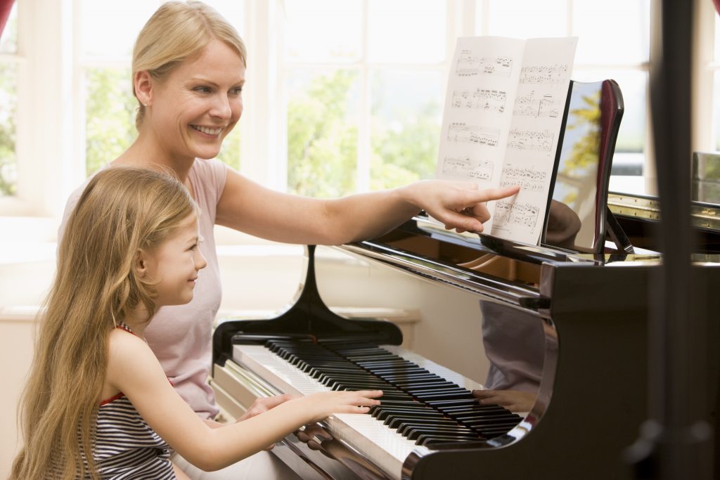 Woman and young girl playing piano and smiling