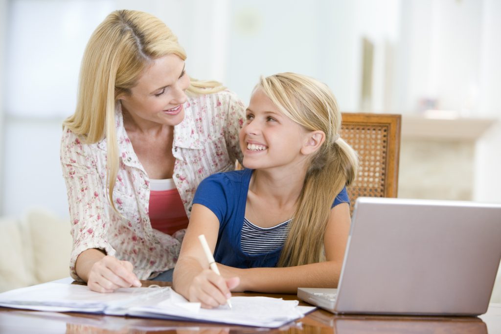 Woman helping young girl with laptop do homework in dining room